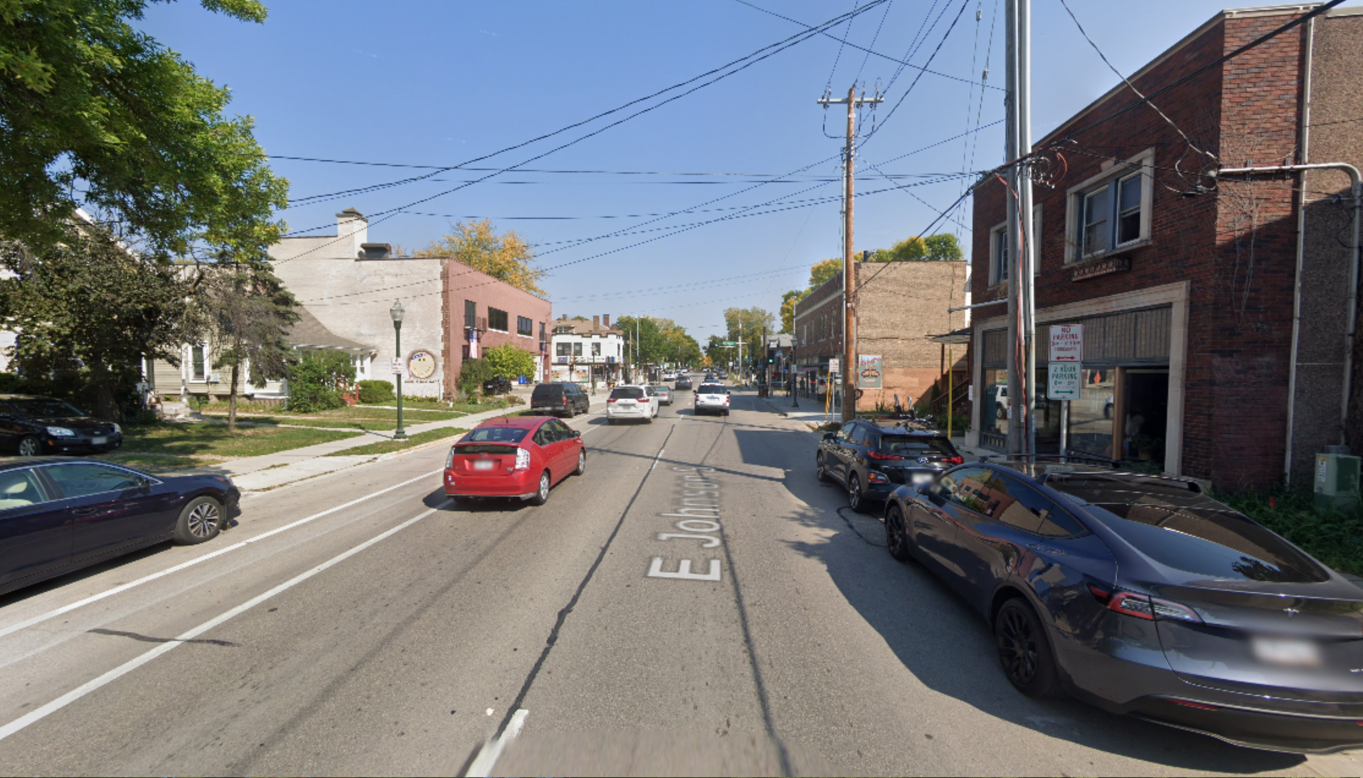 A google street view of a 2 lane one-way road with many cars and many parked cars.  Very little shade.